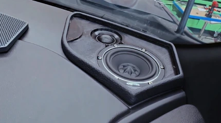 Installer places a subwoofer enclosure into a vehicle trunk during an audio build.